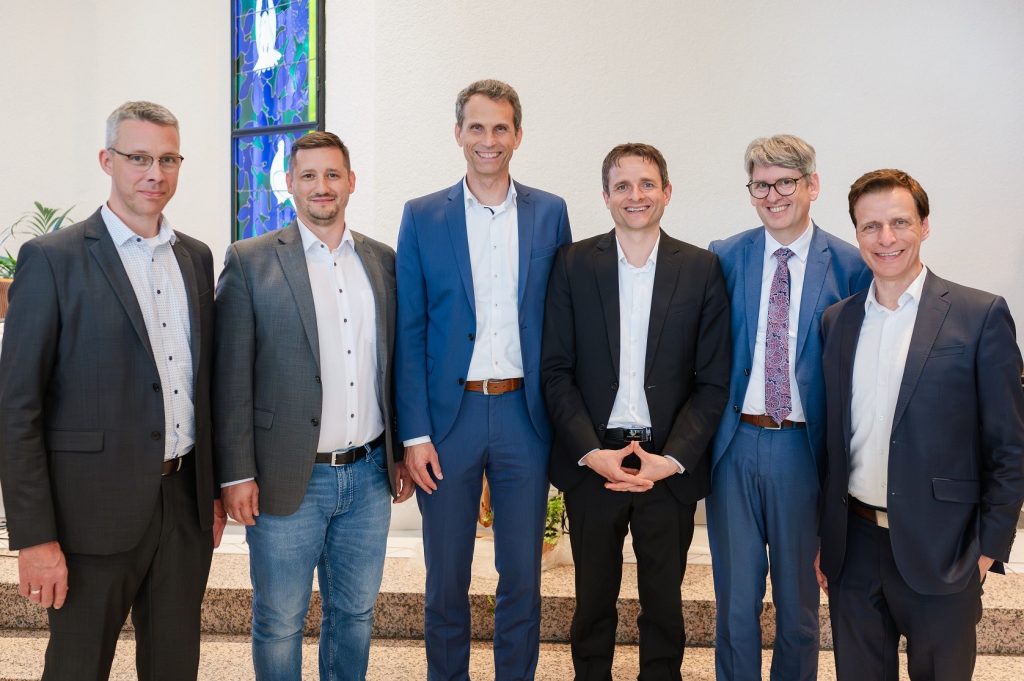 Mannschaftsfoto, sieben Männer in Anzügen vor einem weißem Hintergrund mit bunter Kirchenfenster, professionelle Gruppenaufnahme, Team, Business, Kirche, Gemeinschaft.