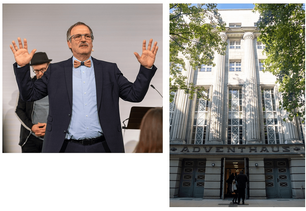 Redner bei Konferenz, humorvoller Mann mit Brille und Fliege, spricht vor Publikum, im Hintergrund ein Mann mit Hut, Business-Event, Präsentation.