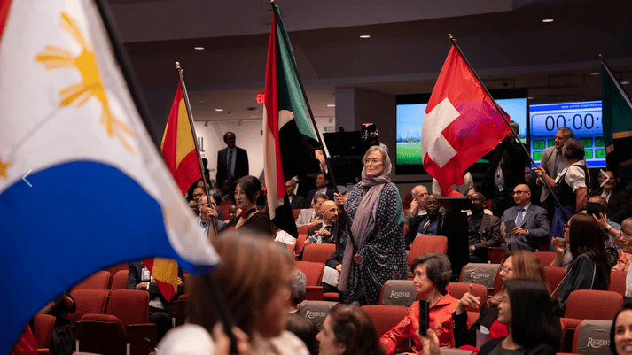 Flaggen verschiedener Nationen bei internationaler Konferenz oder Feier, viele Menschen im Audience, symbolträchtig für globale Zusammenarbeit und kulturelle Vielfalt.